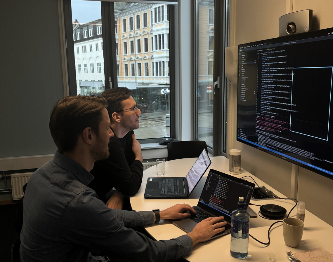 2 menn sitter foran PC og ser på kode